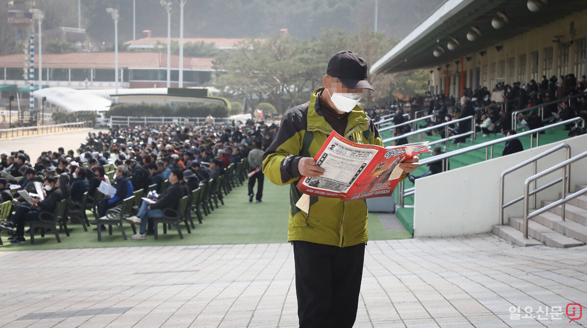 한 노인이 걸음을 멈춘 채 마권과 경마분석지를 보며 고민하고 있다.