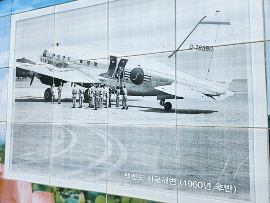 백령도 사곶해변에 1960년대 후반 비행기가 착륙해 있는 모습. 백령면사무소 근처 담장에는 천연비행장이었던 사곶해변을 담은 과거 사진이 벽화로 그려져 있다. 사진=남경식 기자