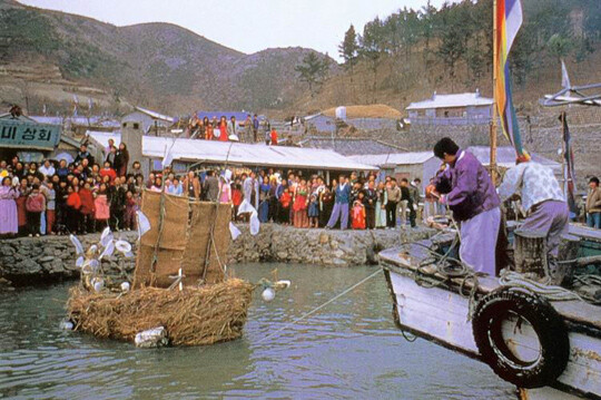 선착장에 온 주민들이 모여 있는 가운데 모선이 띠배를 이끌고 먼 바다로 향하고 있다. 사진=국가유산청 제공