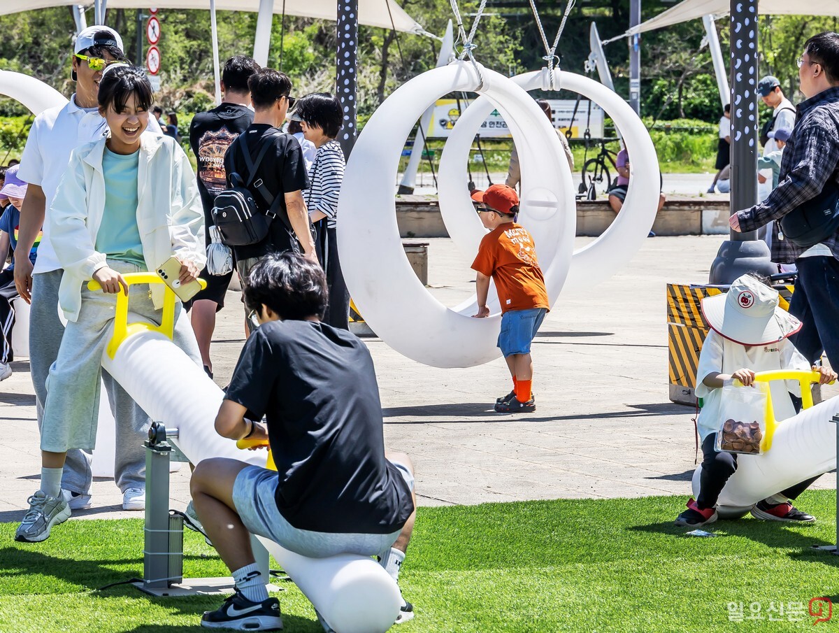 어린이들이 독특한 모양의 원형 그네와 시소를 즐기고 있다.