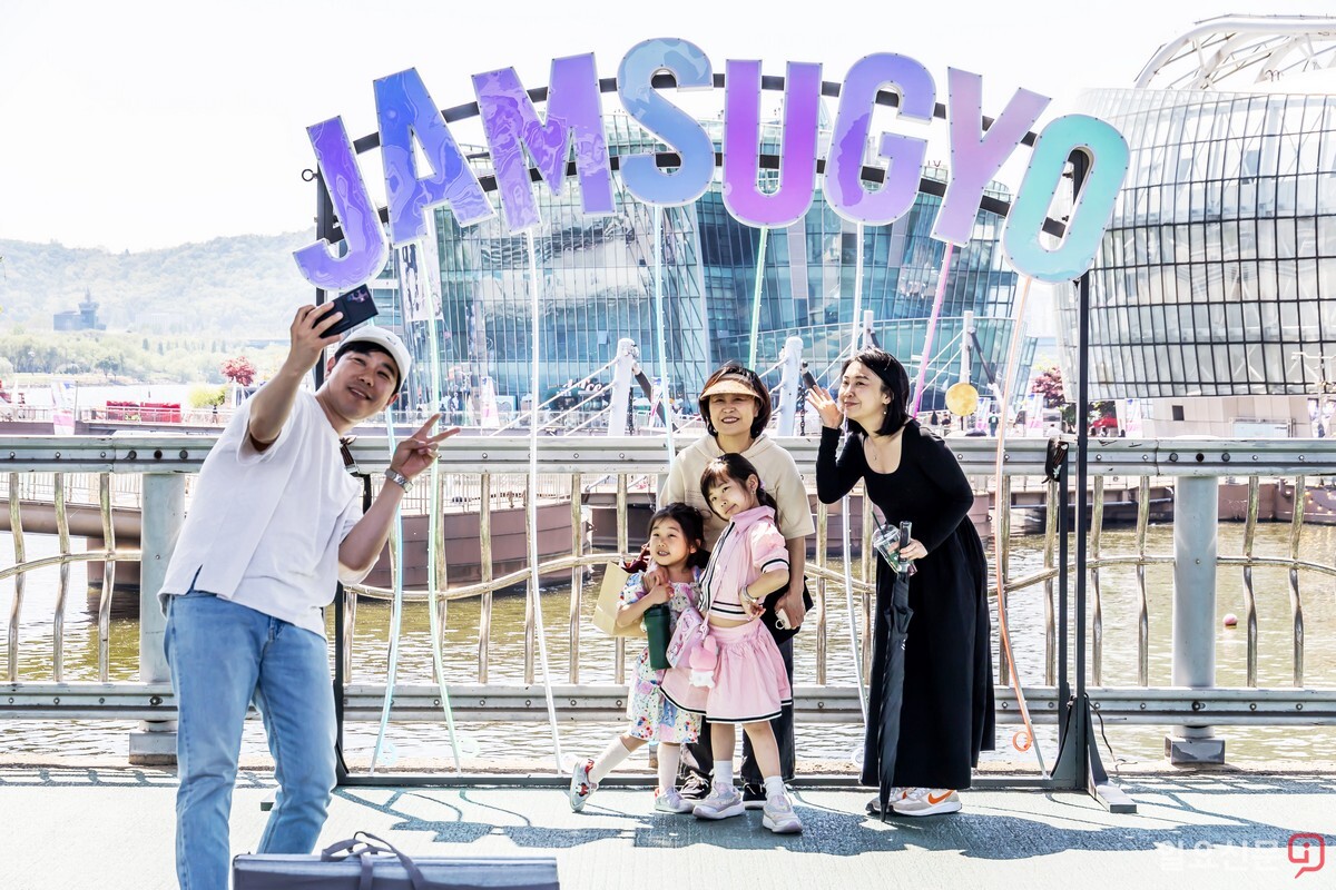 한 가족이 'JAMSUGYO' 조형물을 배경으로 셀카를 찍고 있다.