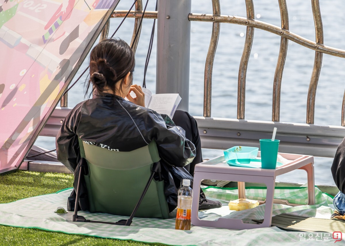 한 시민이 캠핑 의자에 앉아 여유롭게 책을 읽고 있다.