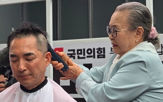 부산 북구 갑 보궐선거에 출마한 박민식 국민의힘 후보 어머니가 5월 21일 오후 부산 북구 구포시장 쌈지공원에서 열린 부산 북구 원팀 출정식에서 아들 머리를 직접 깎아주고 있다. 사진=박민식 후보 선거사무소 제공